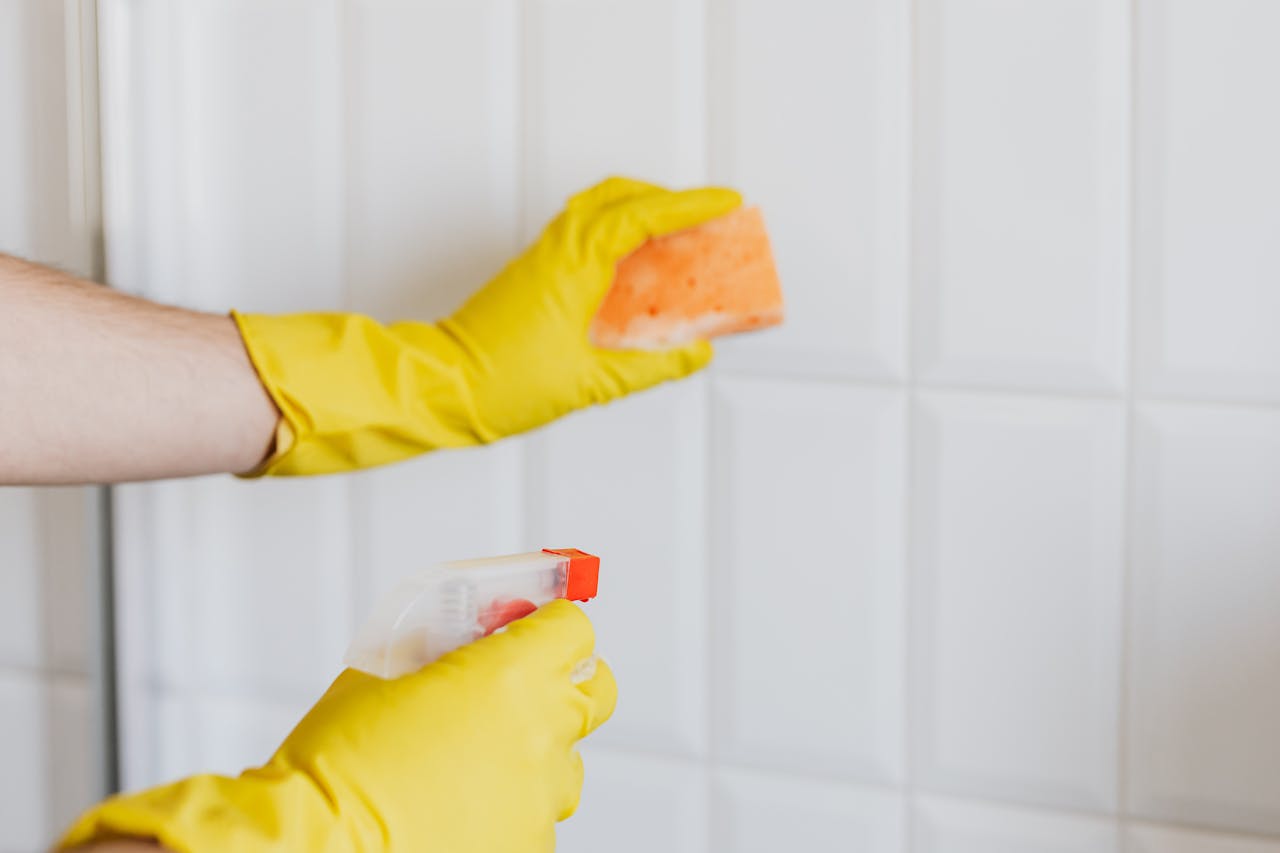 hero-02 Crop unrecognizable woman in yellow rubber gloves cleaning white tiles with spray and soapy sponge